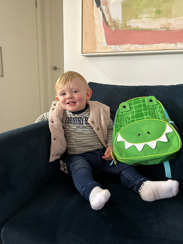 Flynn sitting on his sofa next to a green dinosaur backpack