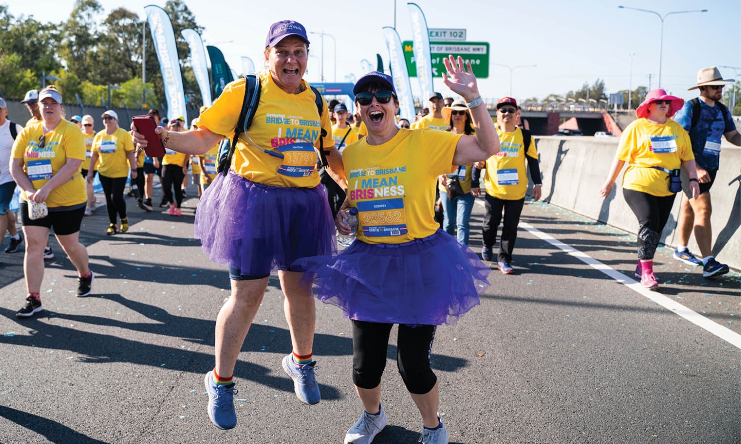 Two people are celebrating as they run Bridge to Brisbane in purple tutus and hats Two people are celebrating as they run Bridge to Brisbane in purple tutus and hats