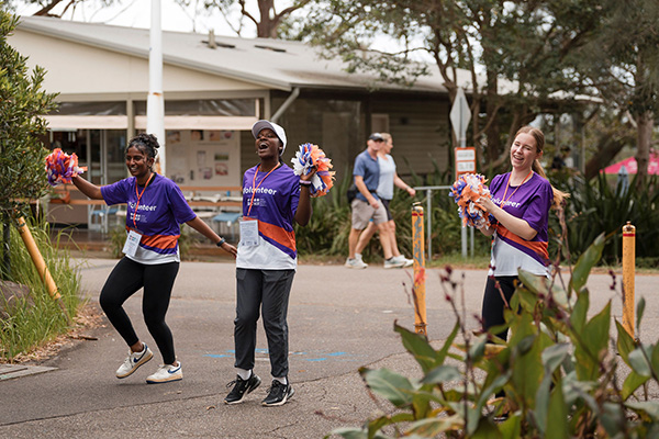 Three Walk for Kids with Cancer volunteers cheering and holding bright coloured pompoms