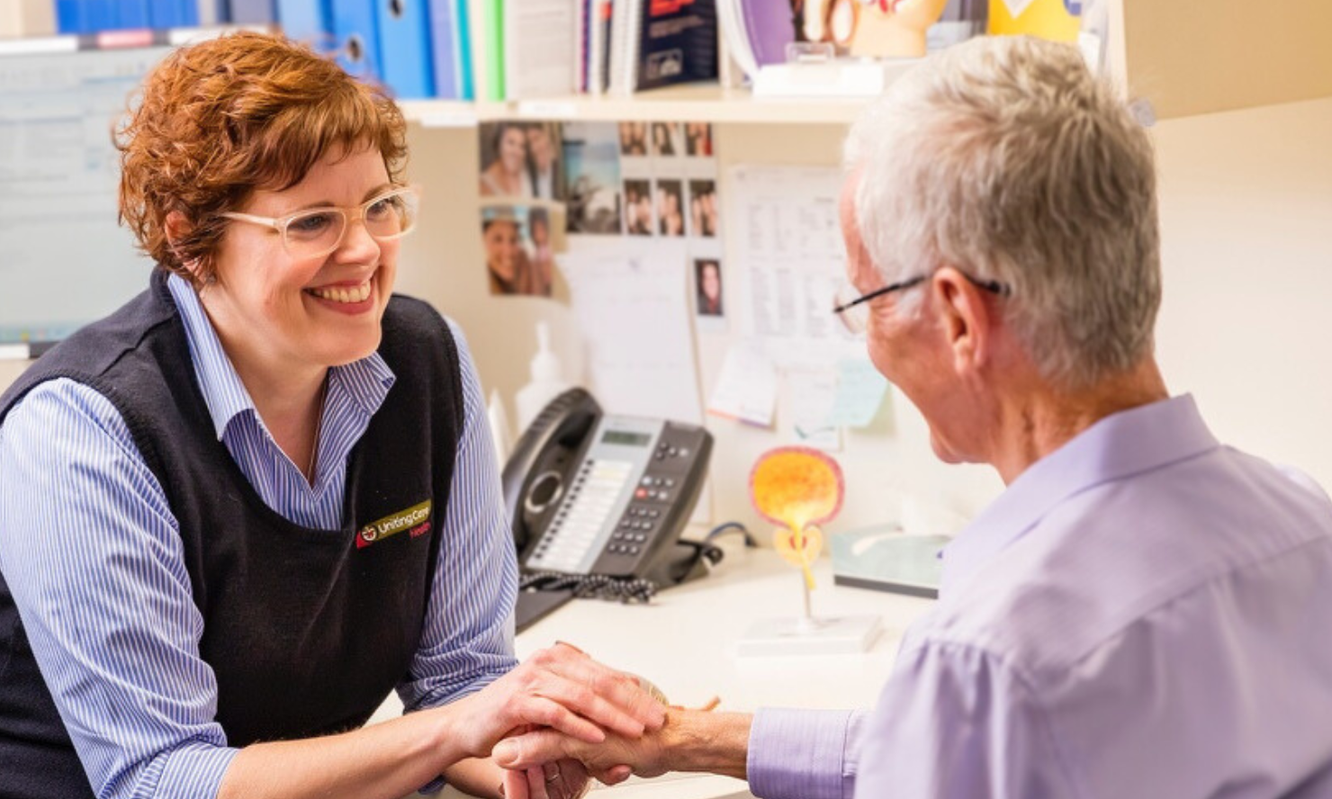 A photo of a healthcare team member gently holding the hand of a patient as they chat together A photo of a healthcare team member gently holding the hand of a patient as they chat together