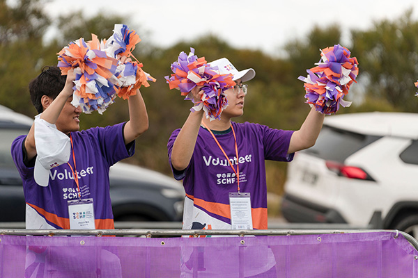 Two Walk for Kids with Cancer volunteers at the finish line cheering on walkers with coloured pompoms