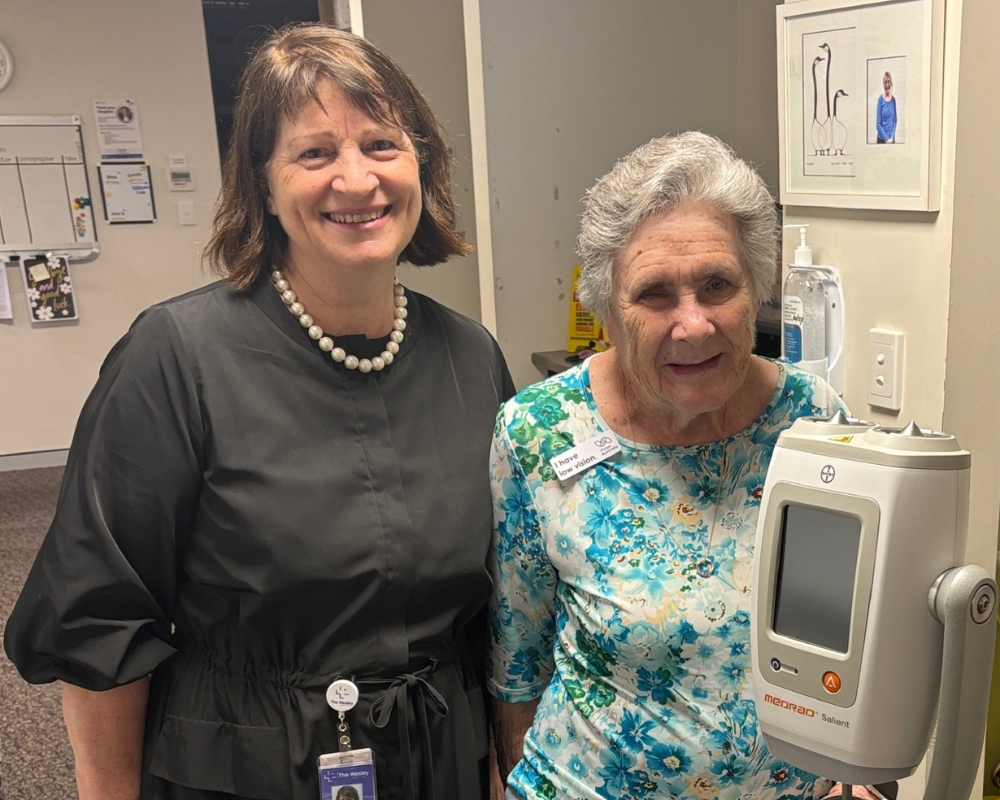 Dr Anne Day and Maureen are standing together in the hallway of the Breast Clinic. They're both smiling warmly.