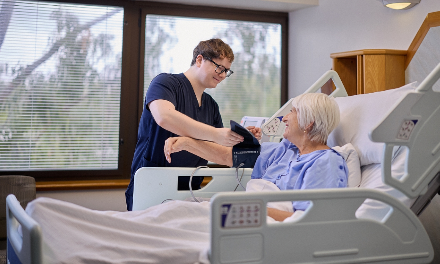 A healthcare professional takes a patient's blood pressure in a hospital room.
